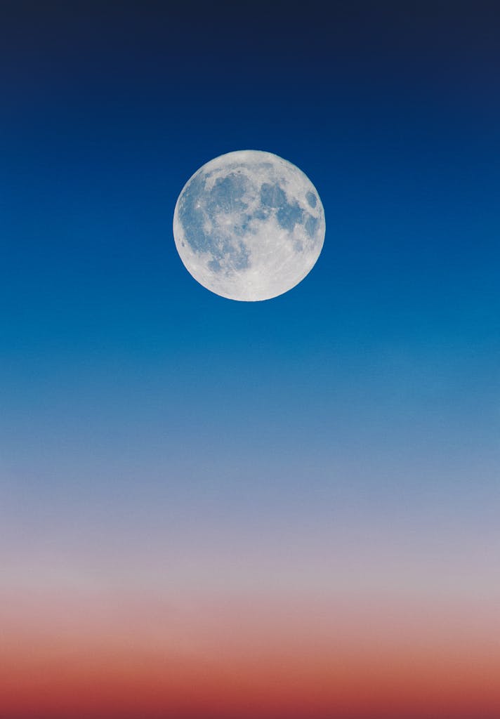 A serene full moon set against a gradient twilight sky, blending hues of blue and orange.